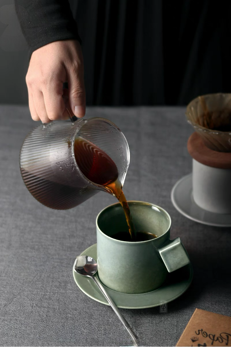 Green ceramic cup and saucer set with coffee being poured from glass carafe highlighting daily coffee ritual use