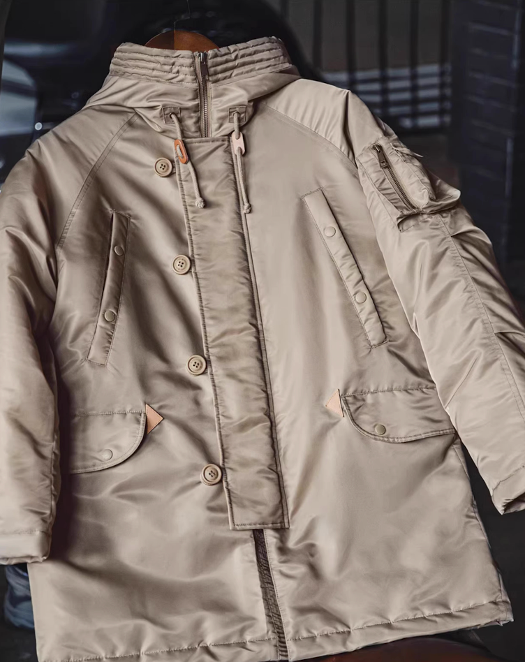 Beige N-3B military parka hanging on wooden hanger in indoor light.