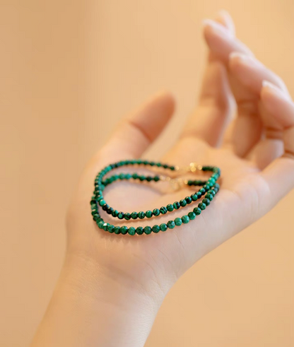 Green malachite bracelets displayed in hand showing dual styles with smooth and faceted beads under warm lighting
