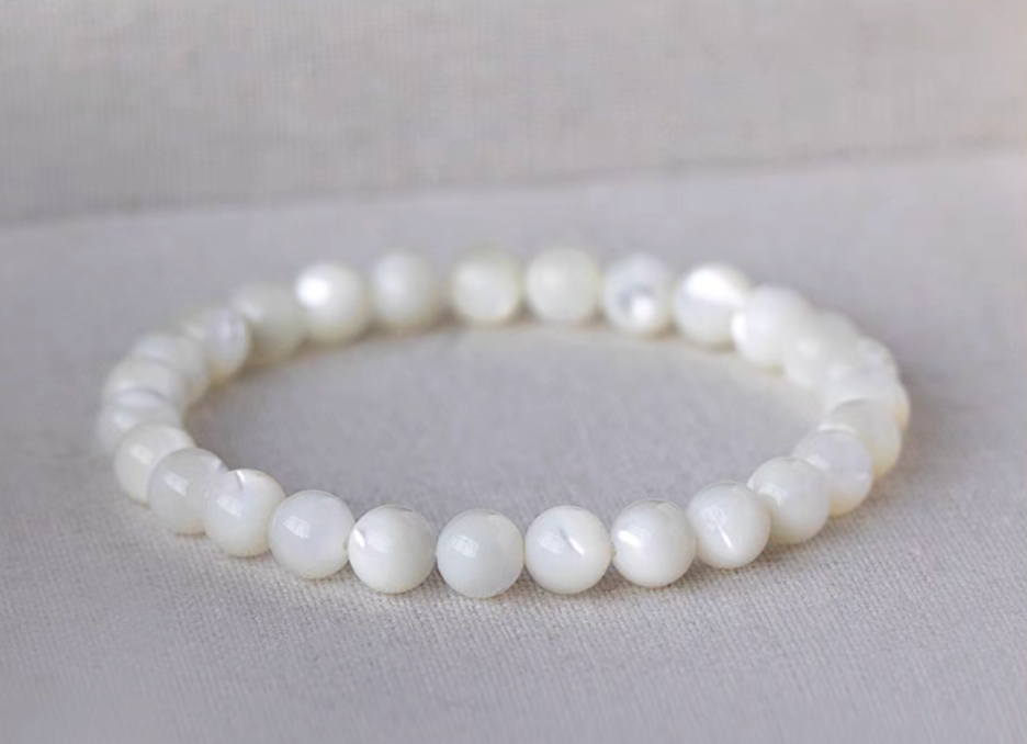 Natural white mother-of-pearl bracelet with round beads arranged in a circle on a light linen surface