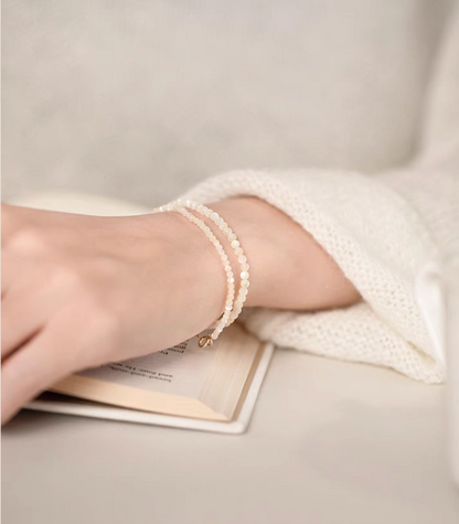 Natural white mother-of-pearl bracelets styled in a double-wrap look on a wrist beside an open book