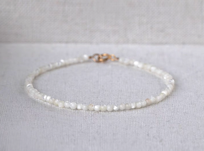 Natural white mother-of-pearl delicate bracelet displayed on fabric with a visible gold clasp and circular shape
