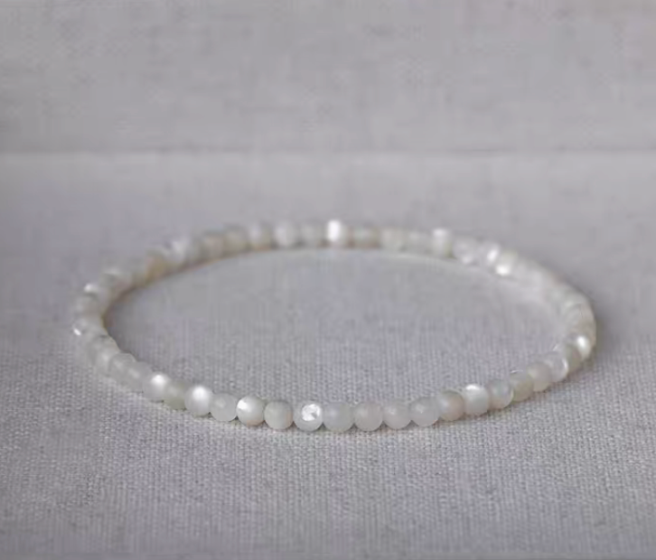 Natural white mother-of-pearl bracelet with smaller beads arranged in a circle on light linen fabric
