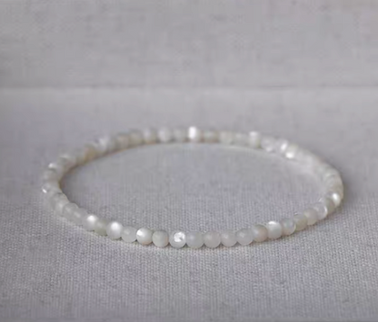 Natural white mother-of-pearl bracelet with smaller beads arranged in a circle on light linen fabric