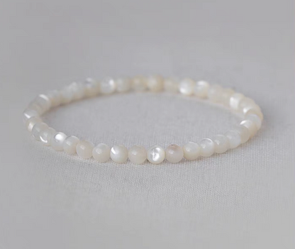 Natural white mother-of-pearl round bead bracelet displayed in a circular shape on pale fabric background