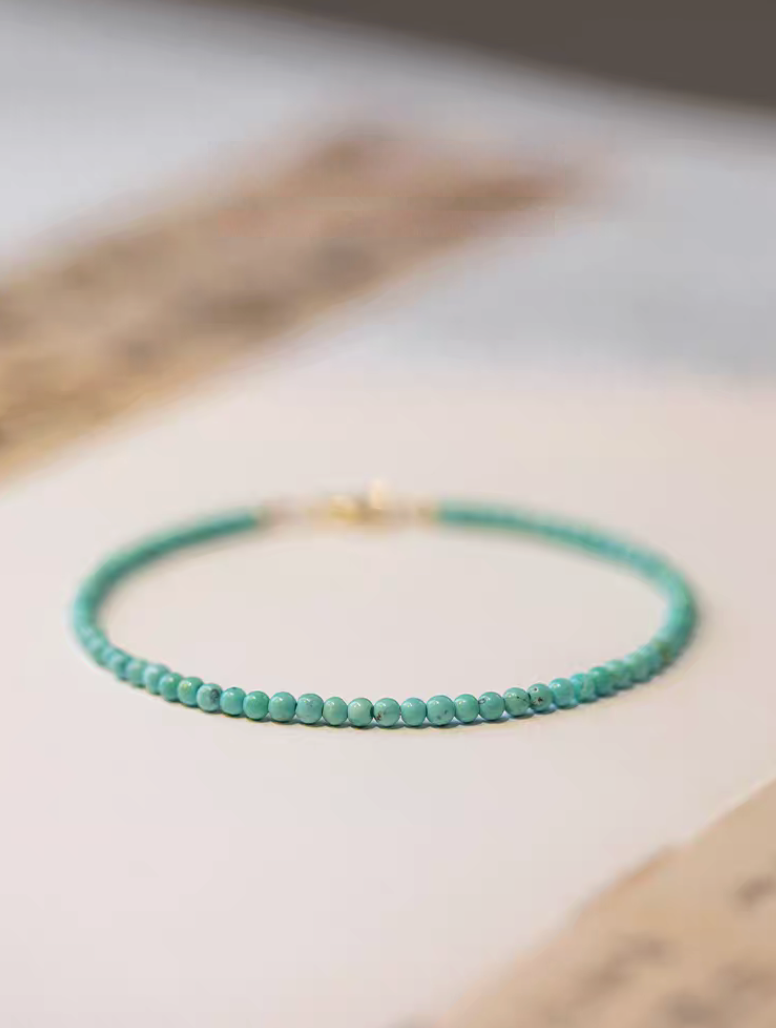 Natural turquoise bracelet with 2mm beads arranged in a circle on paper surface with soft neutral background