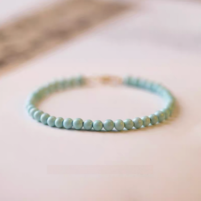 Natural turquoise bracelet with 3.5mm beads arranged in a circle on paper surface with minimal background