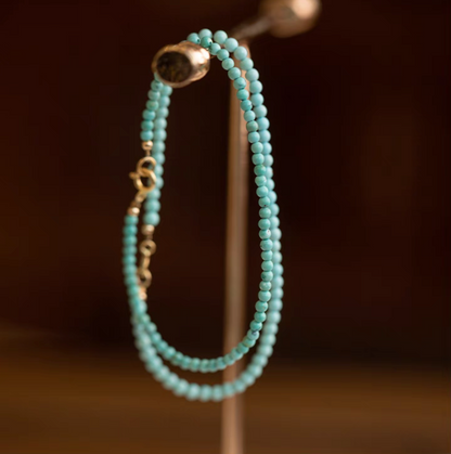 Natural turquoise bracelets in two bead sizes hanging on display stand showing double strand styling with gold clasp detail