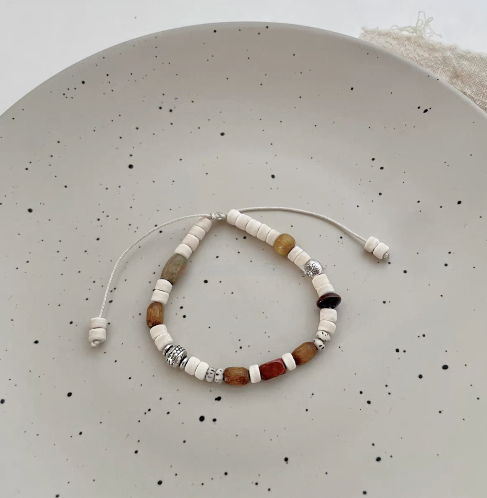 natural wood bead adjustable bracelet with multicolor wooden beads and white drawstring displayed on ceramic plate