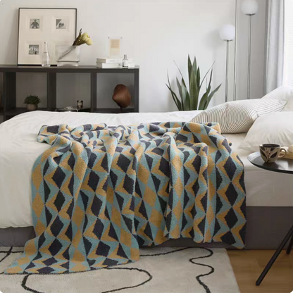 Alonso geometric chenille throw blanket with blue and mustard diamond pattern draped over bed