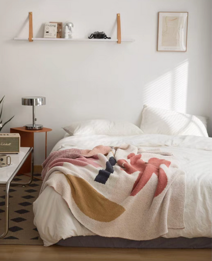 Floral letter chenille throw blanket draped across white bed in a bright minimalist bedroom