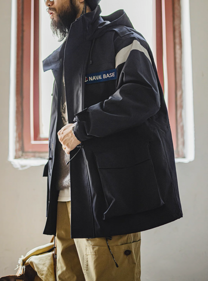 Model standing near window wearing navy reflective hooded parka in natural light
