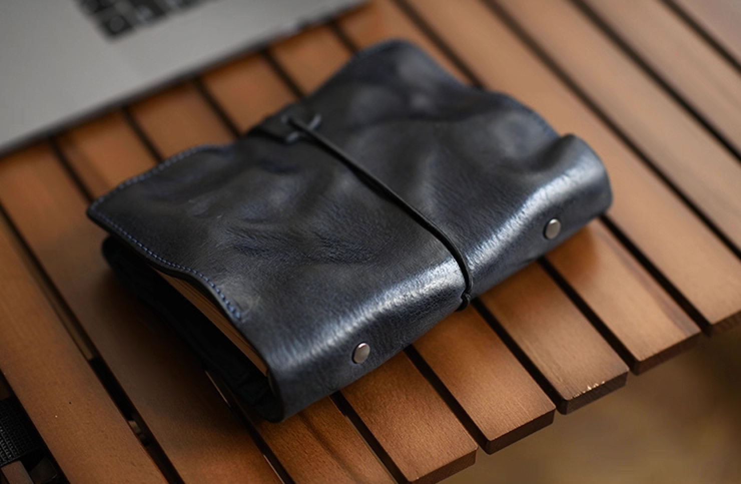 Folded navy leather notebook beside a laptop, highlighting soft patina texture.