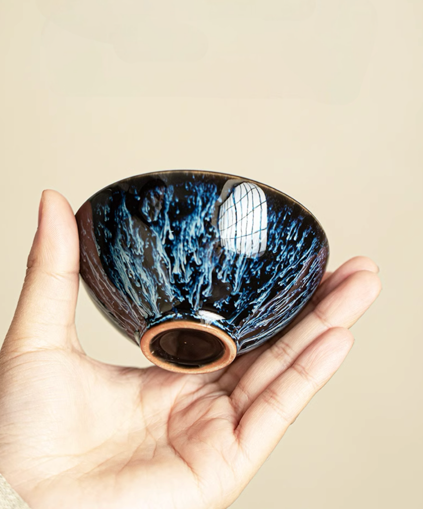 Hand holding blue-black kiln-glazed tea cup showing detailed interior glaze pattern and ceramic craftsmanship