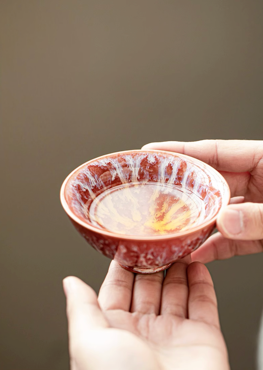 Hand holding red kiln-glazed ceramic tea cup with flowing glaze pattern and warm tone finish