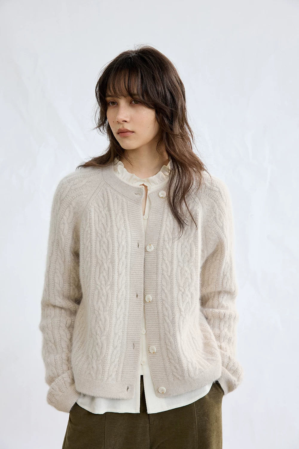 Oatmeal cable-knit cardigan, front view worn open over a blouse
