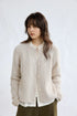 Oatmeal cable-knit cardigan, front view worn open over a blouse