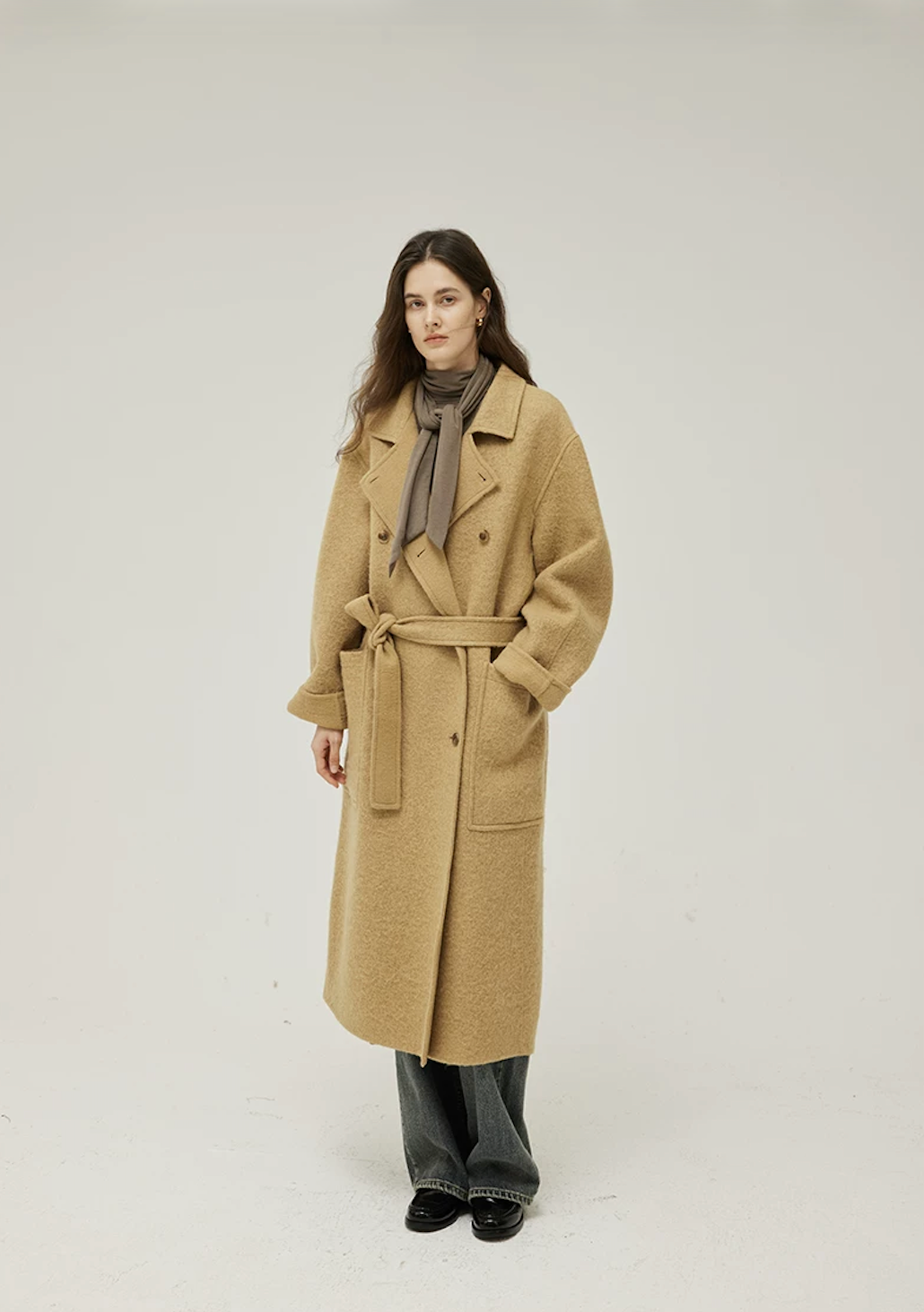 Full-length view of an Ochre long wool coat belted at the waist with cuffed sleeves