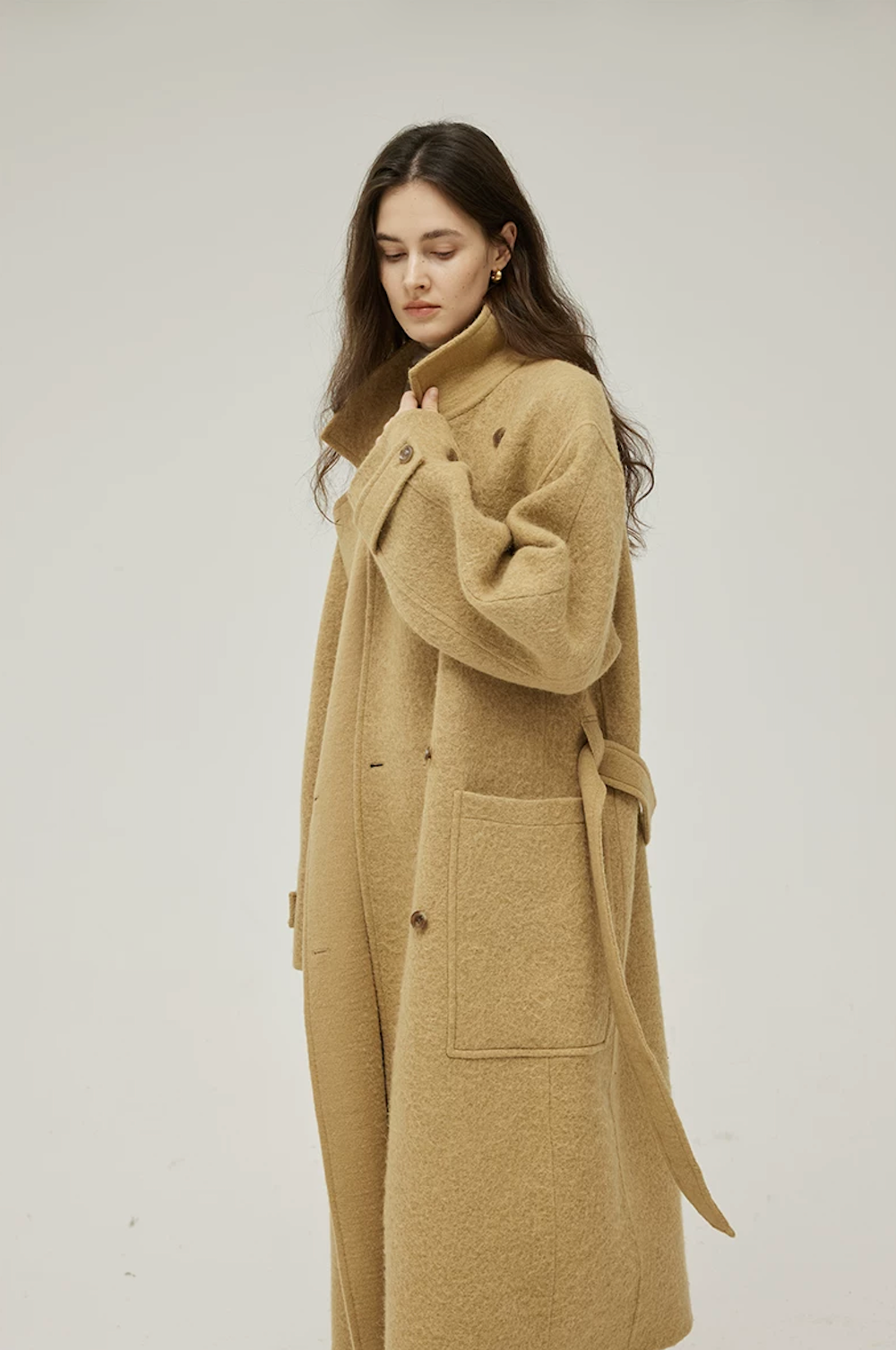 Side view of an Ochre long wool coat with the collar flipped up, low patch pocket, and trailing belt
