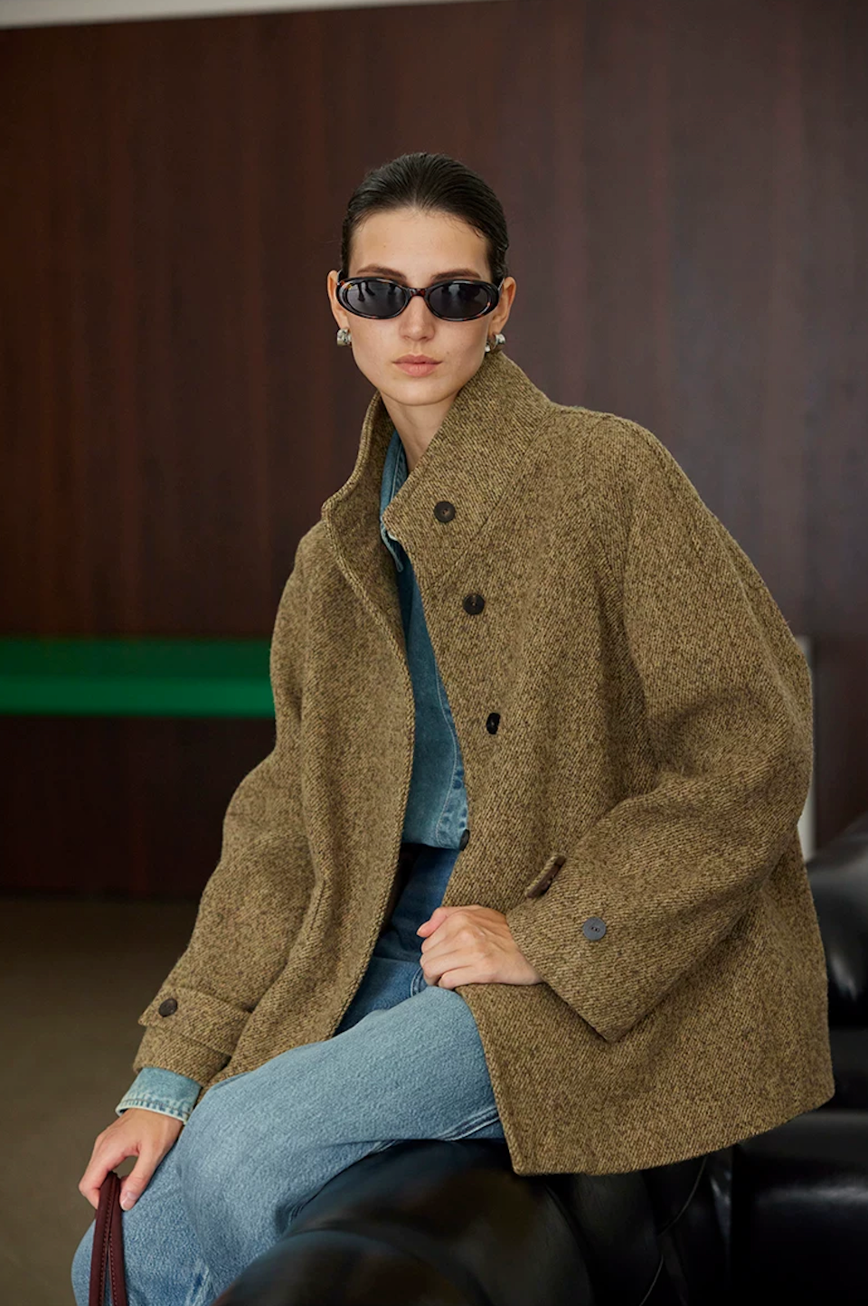 Seated view of an Olive wool tweed jacket with stand collar and buttoned cuff tabs