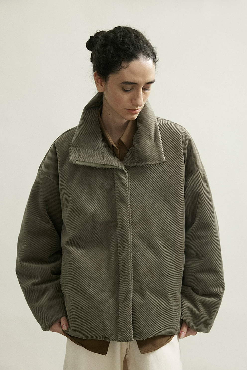 Front view of an Olive Gray boxy corduroy down jacket closed with a concealed placket