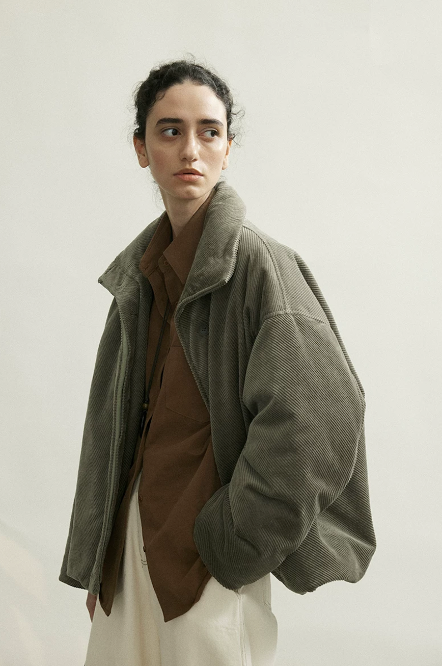 Three-quarter view of an Olive Gray cropped corduroy down jacket with dropped shoulders and full sleeves