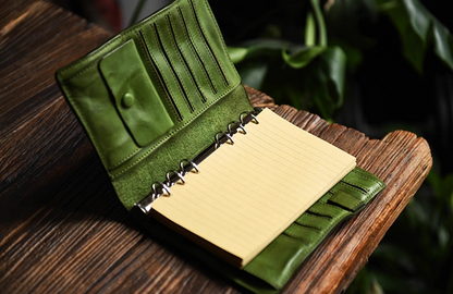Olive green refillable leather notebook fully opened with lined paper on a wood desk.