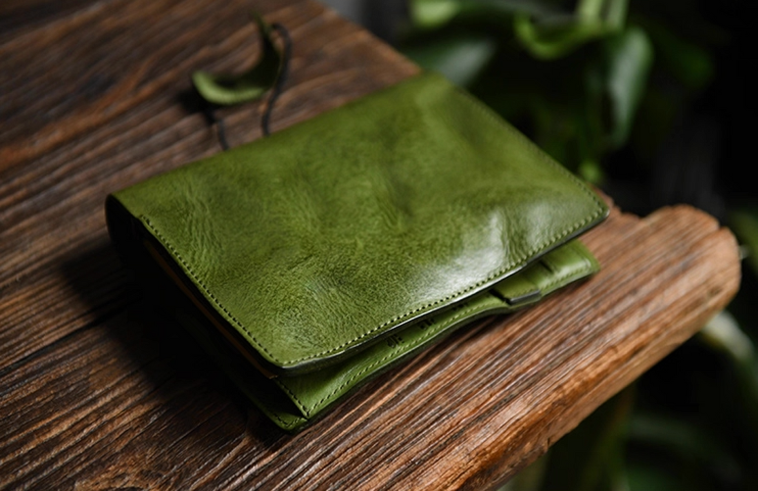 Folded olive leather notebook shown from the side on a wooden surface.