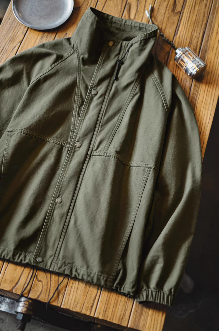 Olive green utility M-65 jacket displayed on wooden table showing front details