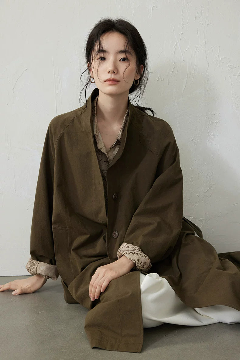 Seated view of an Olive cotton trench coat showing the button front and paisley cuff panels