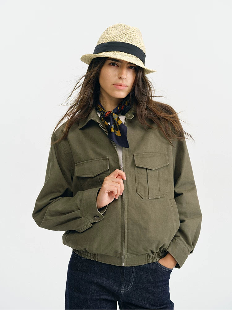 Close-up of an olive utility jacket showing the zip front, flap pockets, and buttoned cuff