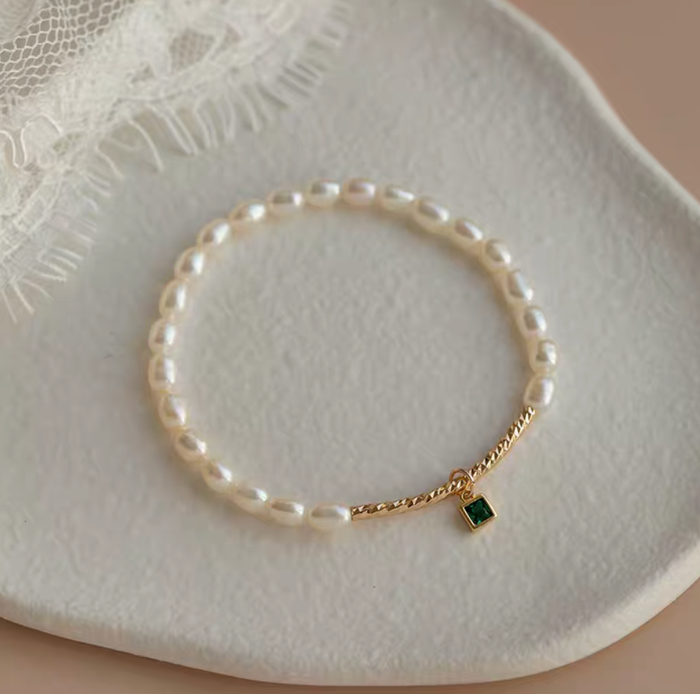 Top view of olivine pearl bracelet with square green gemstone charm and 4mm natural pearls on textured plate.