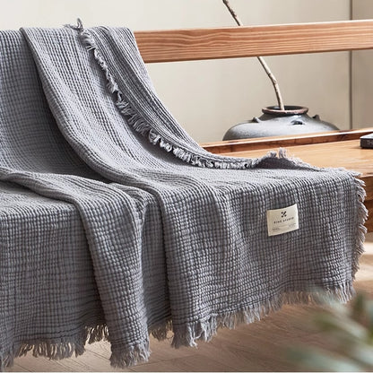 Smoky blue waffle textured organic cotton fringe throw blanket draped across wooden bench in minimalist room.