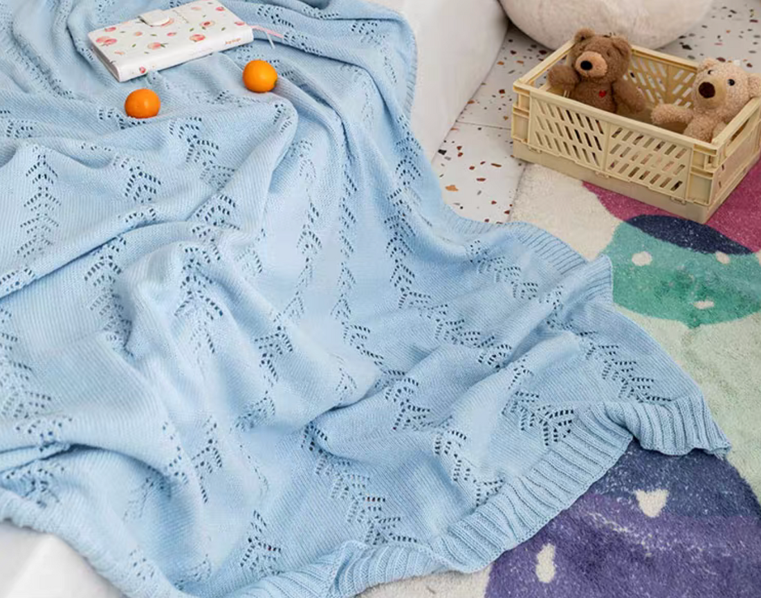 Light Blue Oversize Knit Throw Blanket draped across a sofa with oranges and notebook showing breathable cotton knit leaf pattern