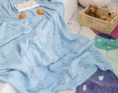 Light Blue Oversize Knit Throw Blanket draped across a sofa with oranges and notebook showing breathable cotton knit leaf pattern