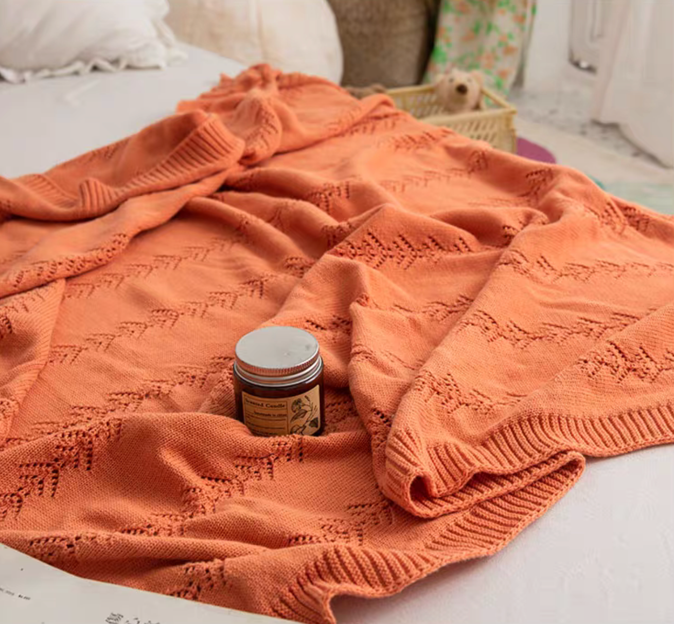 Orange Oversize Knit Throw Blanket spread on bed with candle accent showing decorative knit leaf pattern