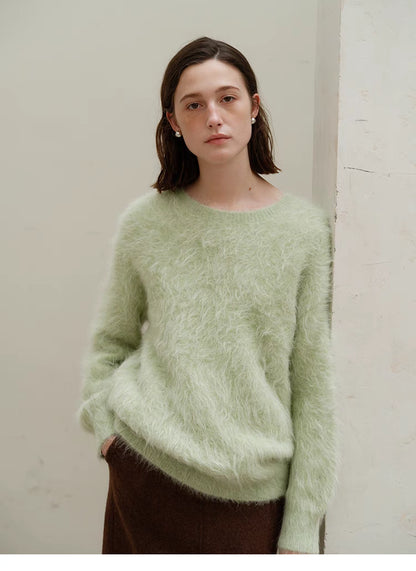 Honeydew green alpaca crewneck sweater front view on model standing by neutral wall, showing relaxed oversized fit and plush texture