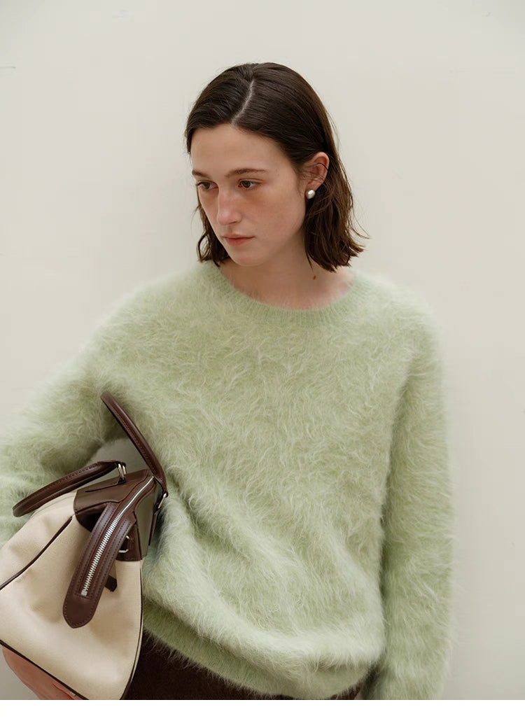 Honeydew green alpaca sweater styled with handbag, close view highlighting soft fibers, crewneck shape and refined casual look