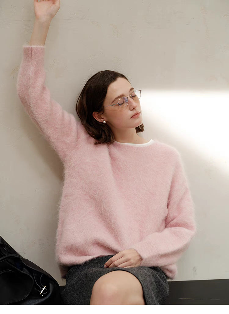 Pink oversized alpaca crewneck sweater worn by model leaning against wall with arm raised, showcasing relaxed fit and soft fuzzy texture
