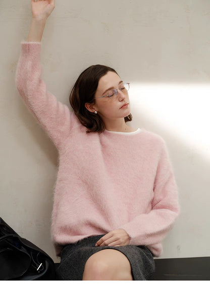 Pink oversized alpaca crewneck sweater worn by model leaning against wall with arm raised, showcasing relaxed fit and soft fuzzy texture
