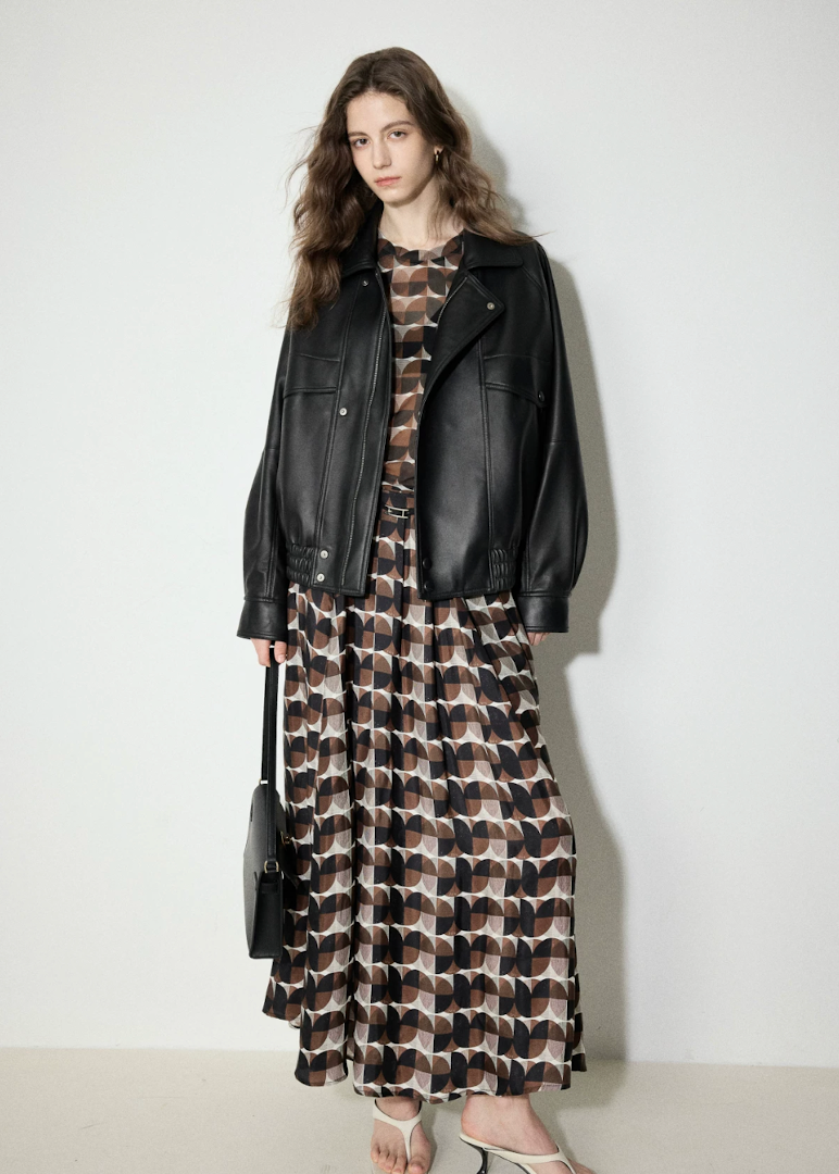 Full-length view of oversized black leather bomber worn open over a long printed dress
