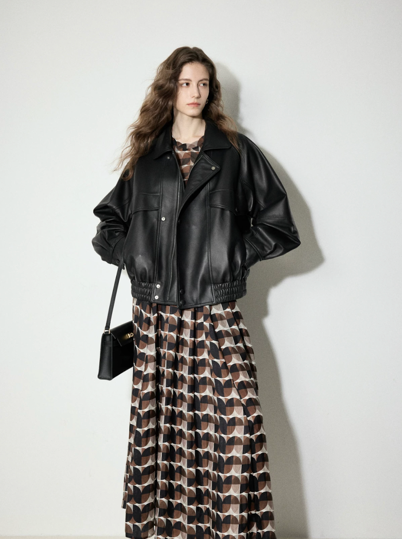 Black lambskin bomber jacket worn over a printed maxi dress, hands in pockets