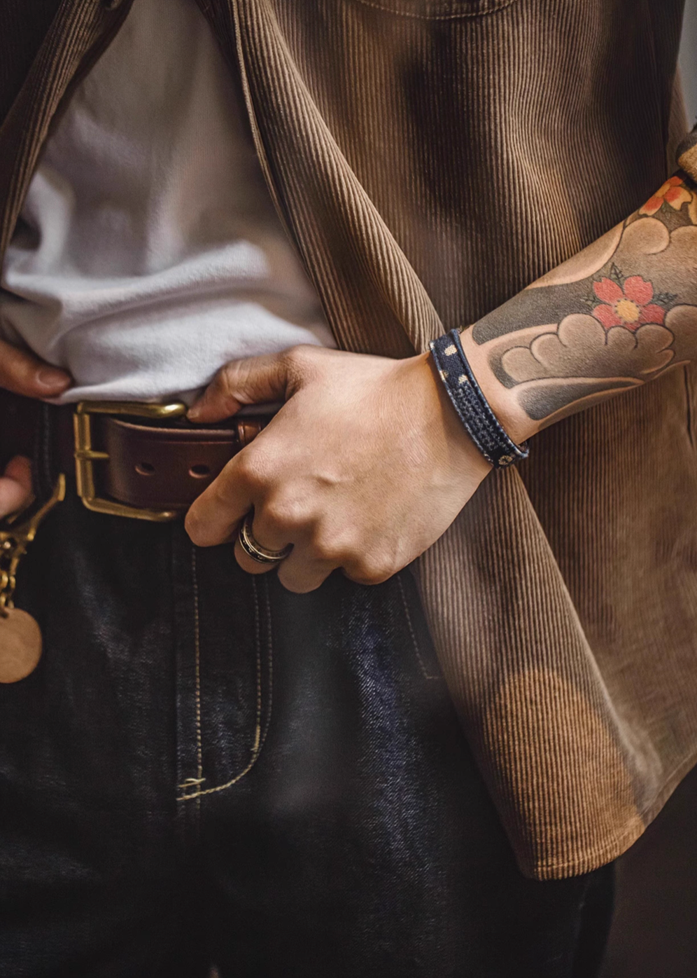 Person wearing patchwork leather bracelet in black and navy blue styled with casual outfit and tattooed arm