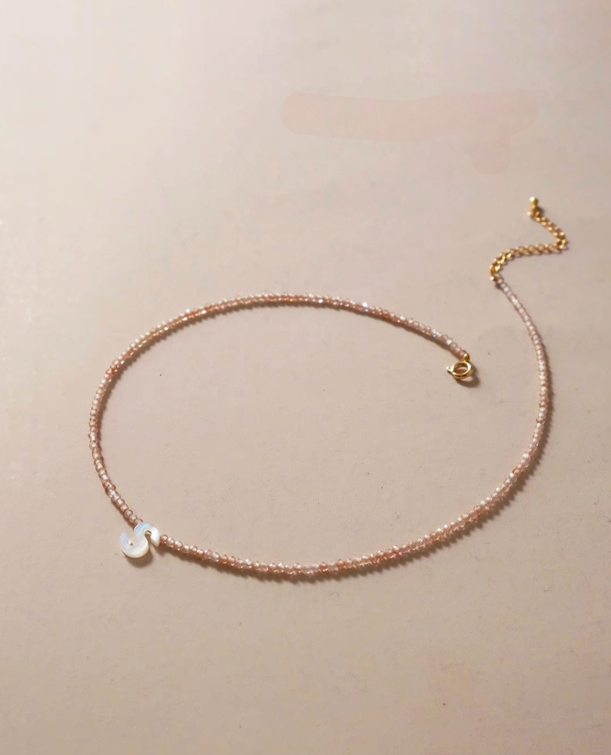 Letter S personalized shell initial necklace on natural beaded chain shown in angled lifestyle close-up