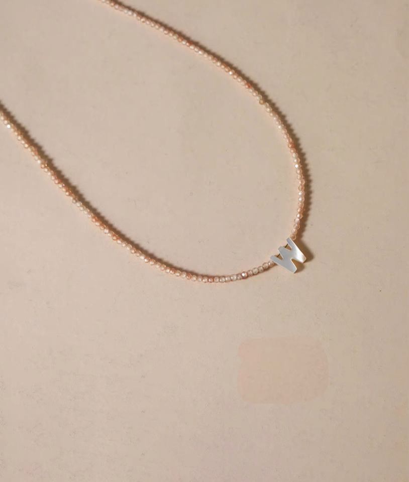 Letter W personalized shell initial necklace displayed on natural background with delicate beaded chain flat lay