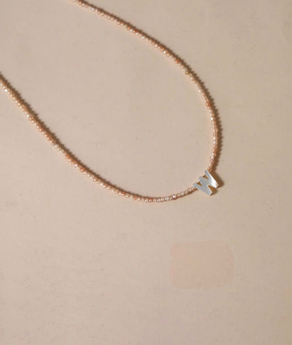 Letter W personalized shell initial necklace displayed on natural background with delicate beaded chain flat lay