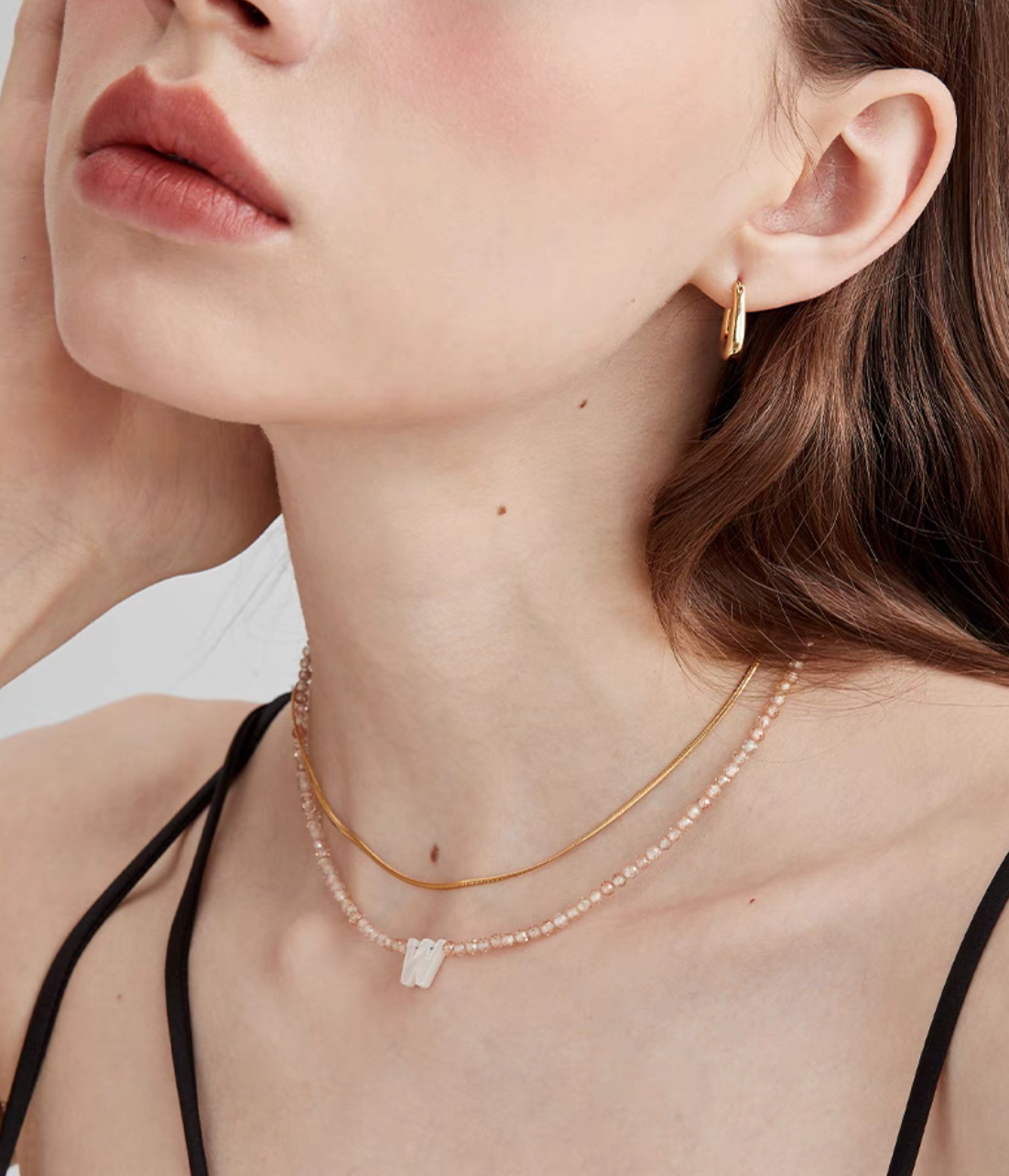Letter W personalized shell initial necklace worn on neck with natural stone beaded chain in lifestyle styling
