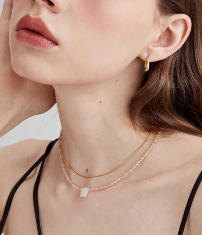 Letter W personalized shell initial necklace worn on neck with natural stone beaded chain in lifestyle styling