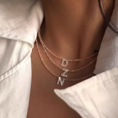 Layered personalized shell initial necklaces with letters D Z N worn on neck featuring natural bead chains