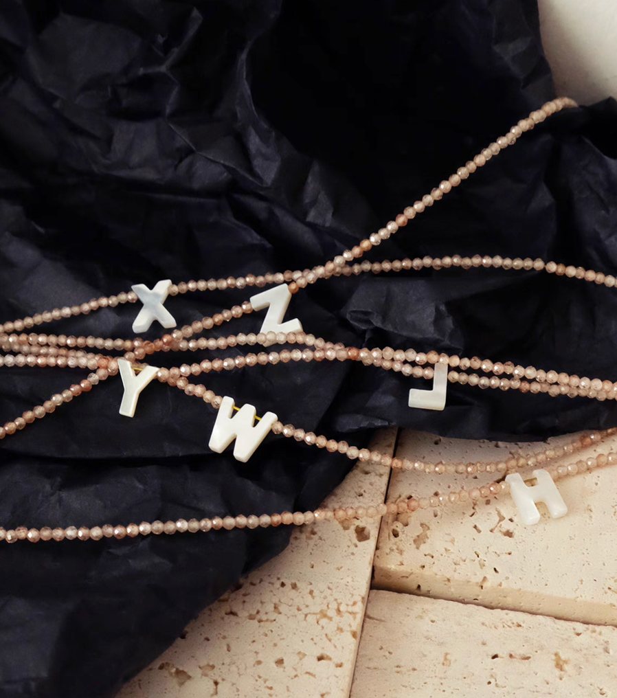 Flat lay of personalized shell initial necklaces with mixed letters on natural stone bead chains stylish arrangement